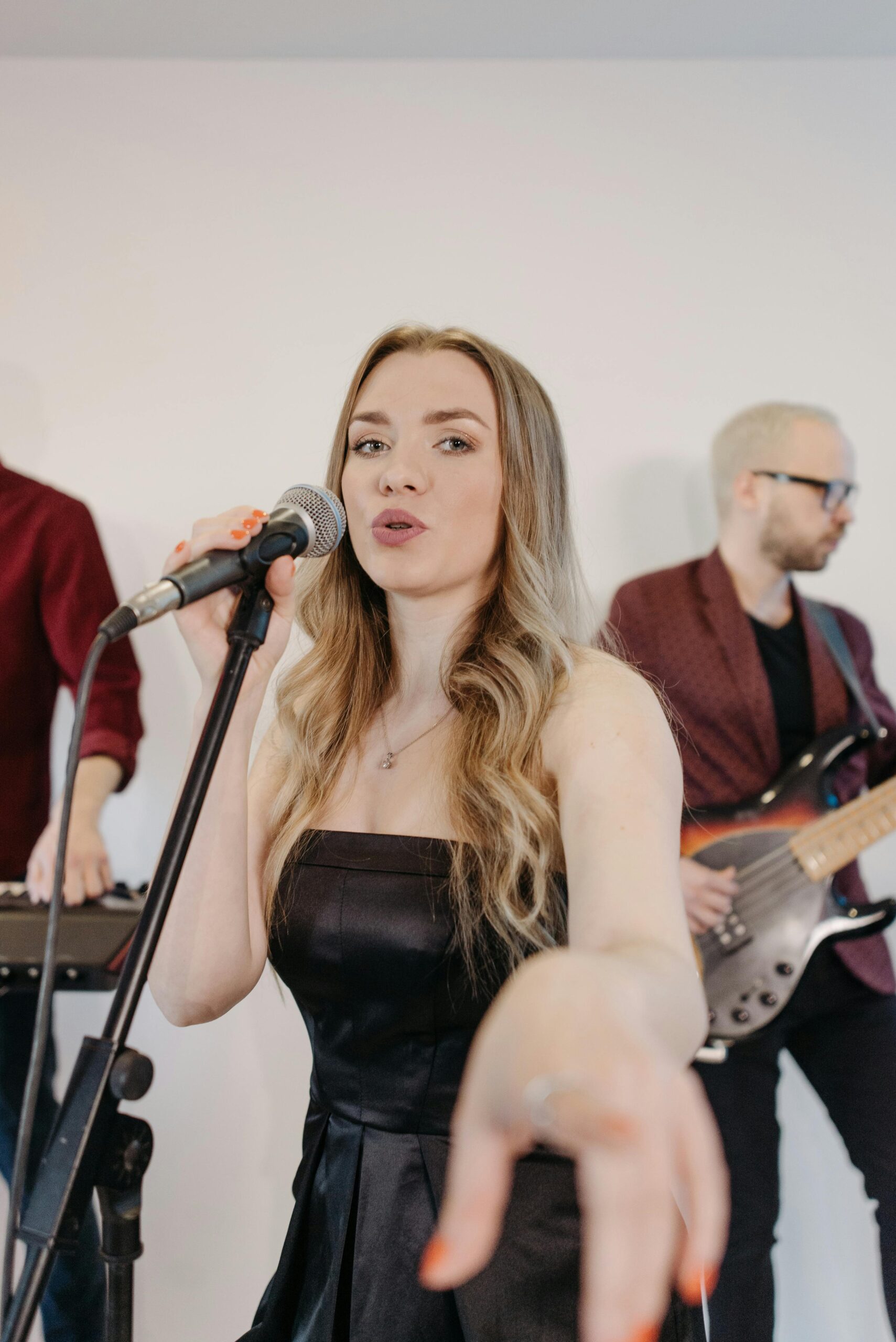 Blonde female vocalist singing at a live band performance indoors, holding a microphone passionately.